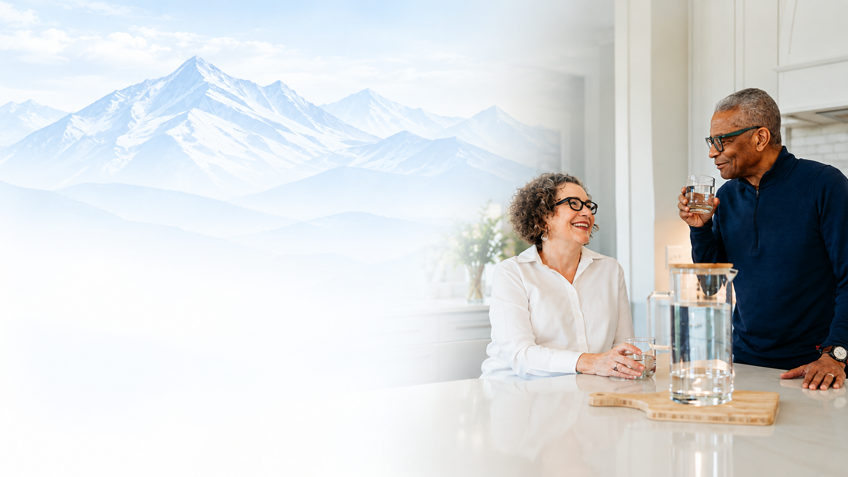 A couple enjoying glasses of filtered water at their kitchen island, with mountains beyond
