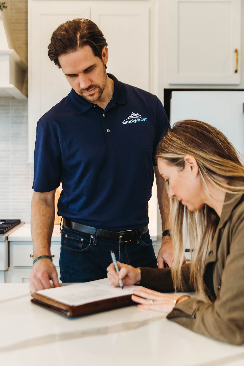 Homeowner signing paperwork with a Simply Water specialist in a home kitchen